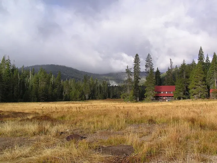 Red buildings of Drakesbad Guest Ranch at the edge of a golden meadow below forested ridges