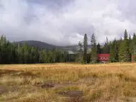 Red buildings of Drakesbad Guest Ranch at the edge of a golden meadow below forested ridges