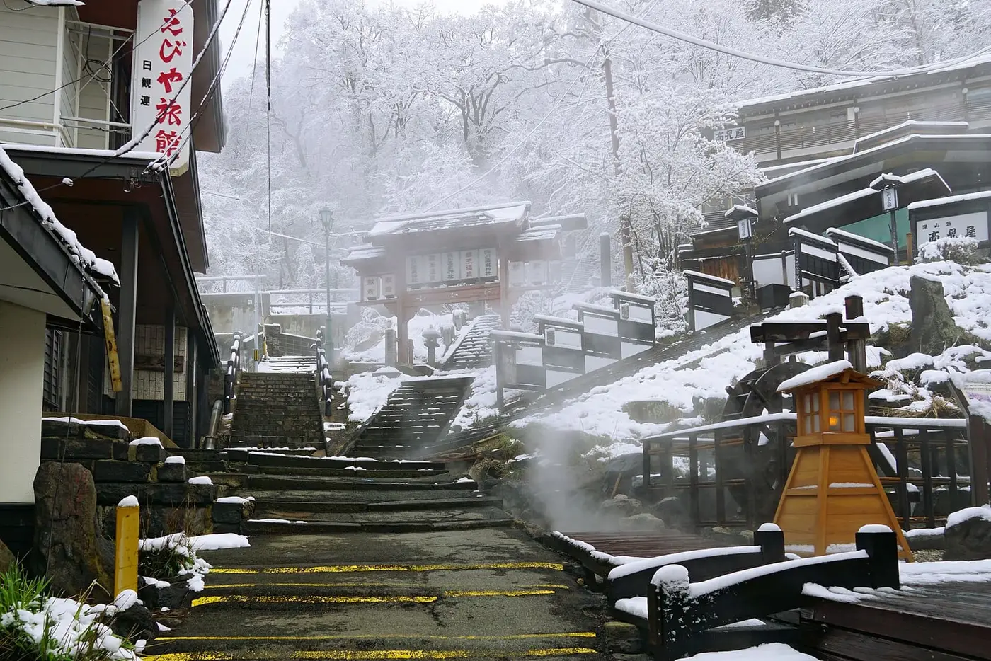 Steam rising over snowy stone steps and buildings in Zao Onsen town