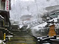 Steam rising over snowy stone steps and buildings in Zao Onsen town