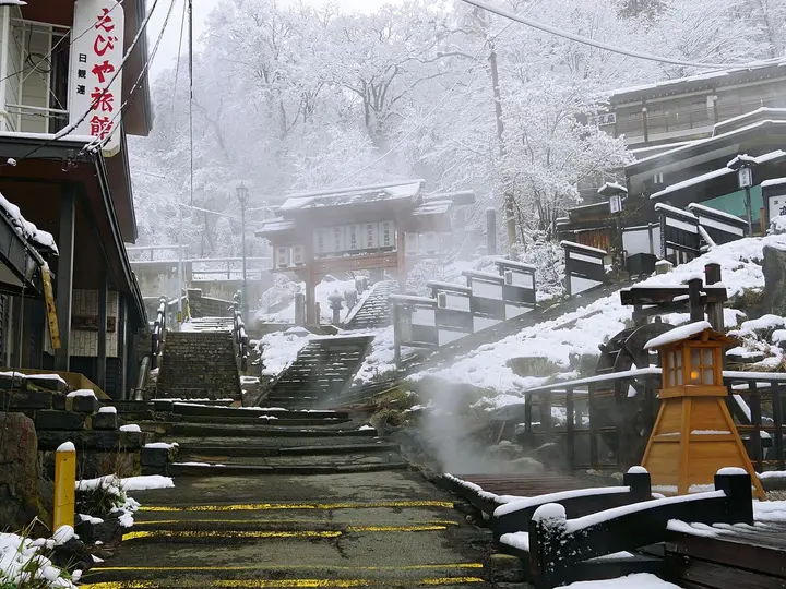Steam rising over snowy stone steps and buildings in Zao Onsen town