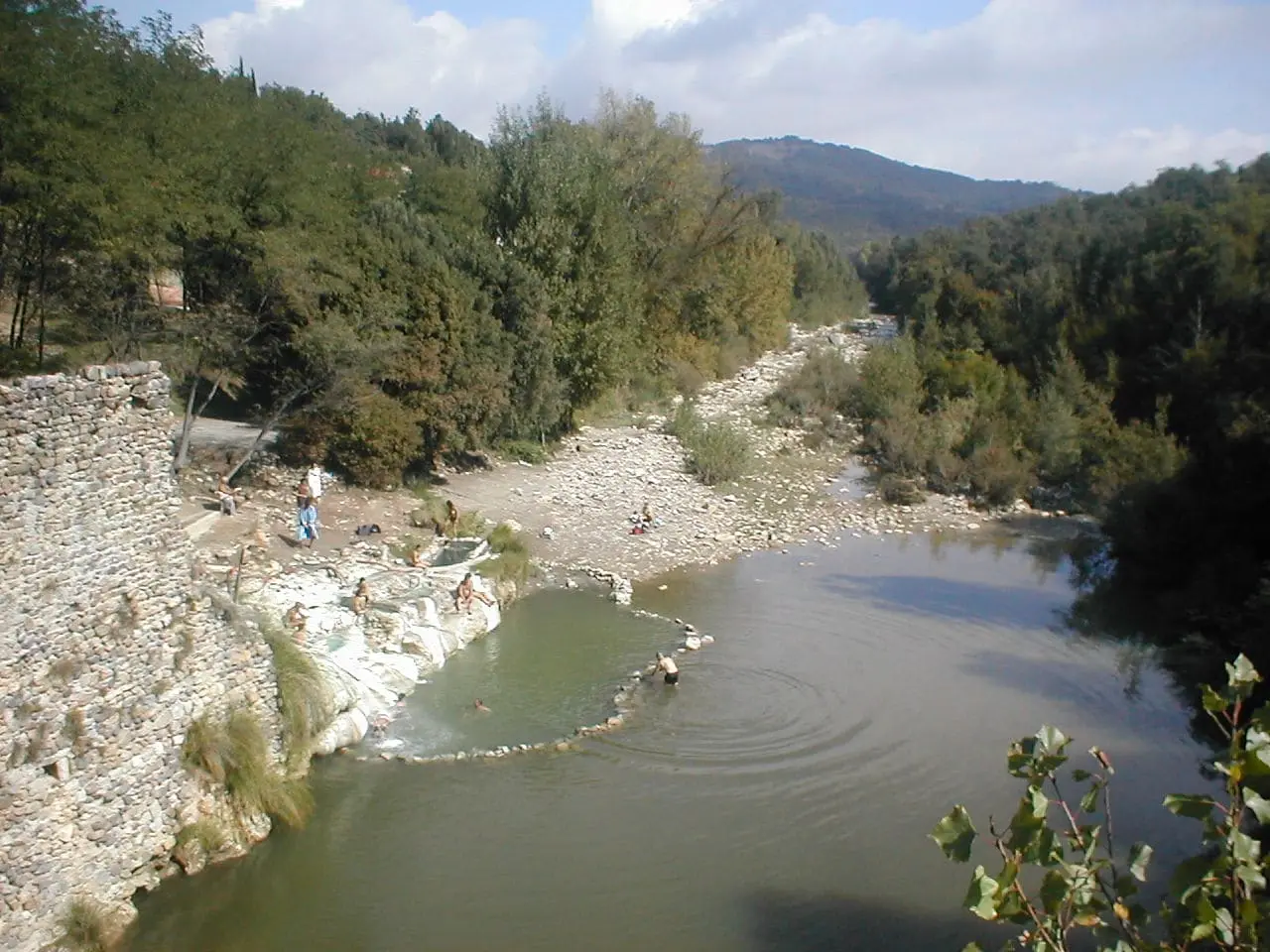 Stone walled hot pools of Terme di Petriolo on the bank of the Farma river below wooded hills