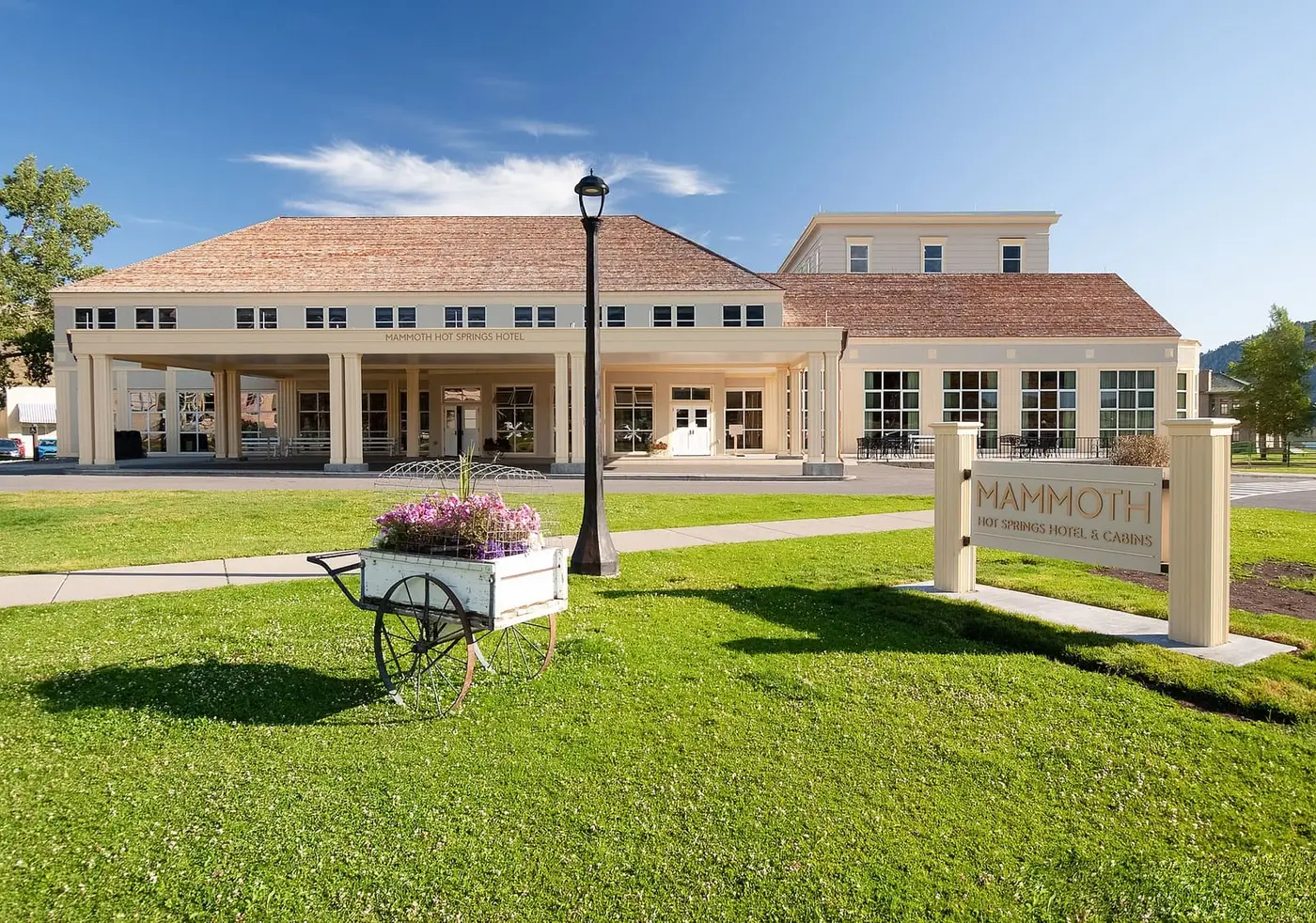 Mammoth Hot Springs Hotel exterior with covered entrance, lawn and Mammoth sign under blue sky