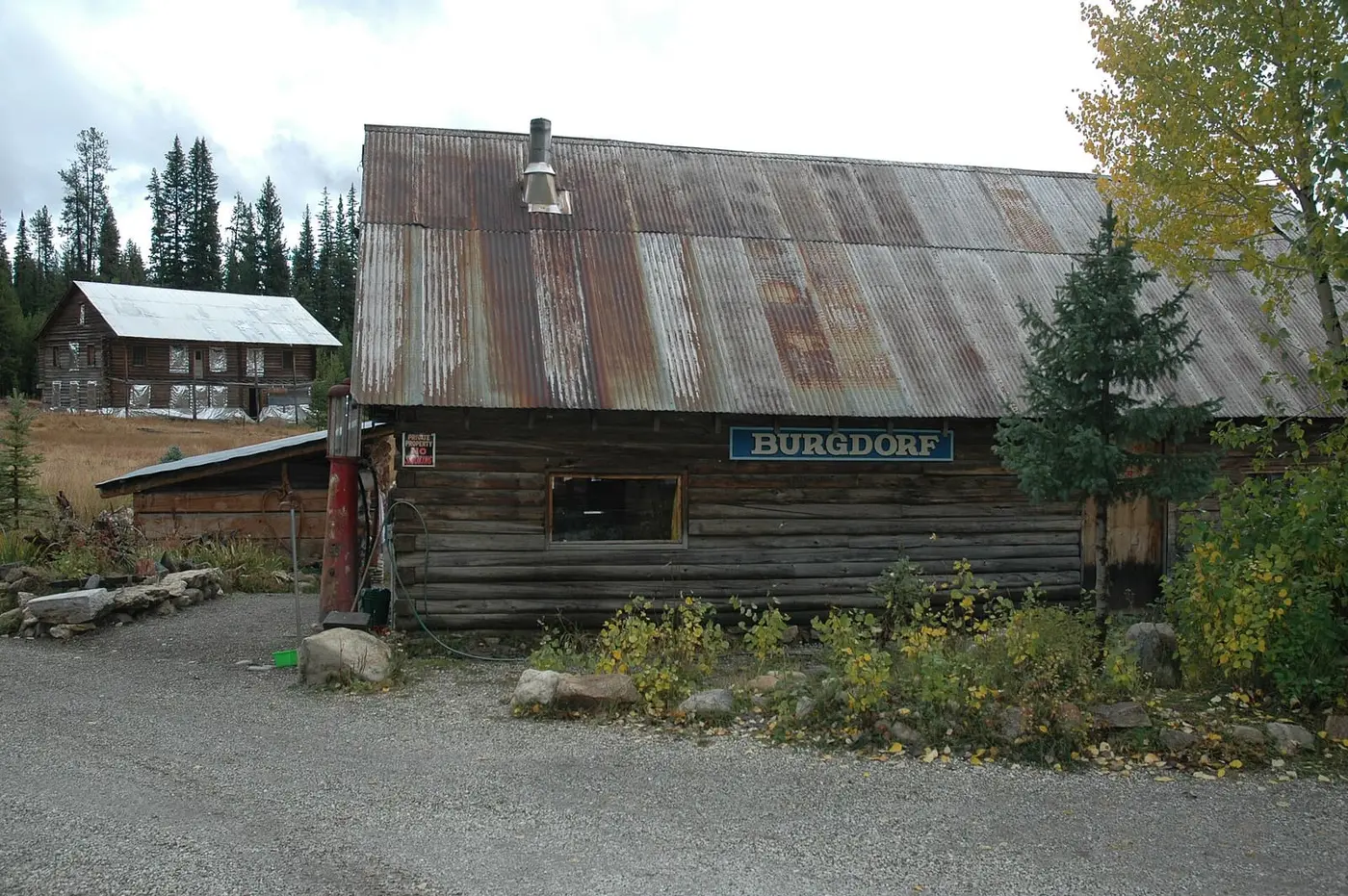 Rustic log lodge with a Burgdorf sign and rusted metal roof beside a gravel lot at Burgdorf Hot Springs