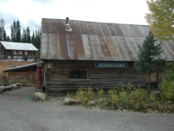 Rustic log lodge with a Burgdorf sign and rusted metal roof beside a gravel lot at Burgdorf Hot Springs