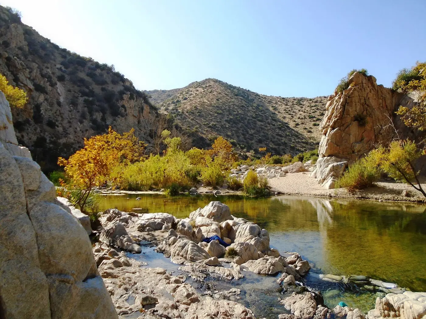 Deep Creek winding between granite boulders and autumn cottonwoods, with small hot spring pools in the foreground