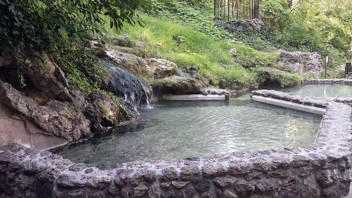 Hot spring water spilling from mossy tufa rock into a stone rimmed pool at the Hot Water Cascade