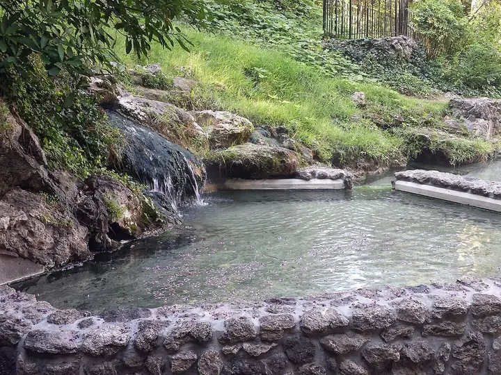 Hot spring water spilling from mossy tufa rock into a stone rimmed pool at the Hot Water Cascade