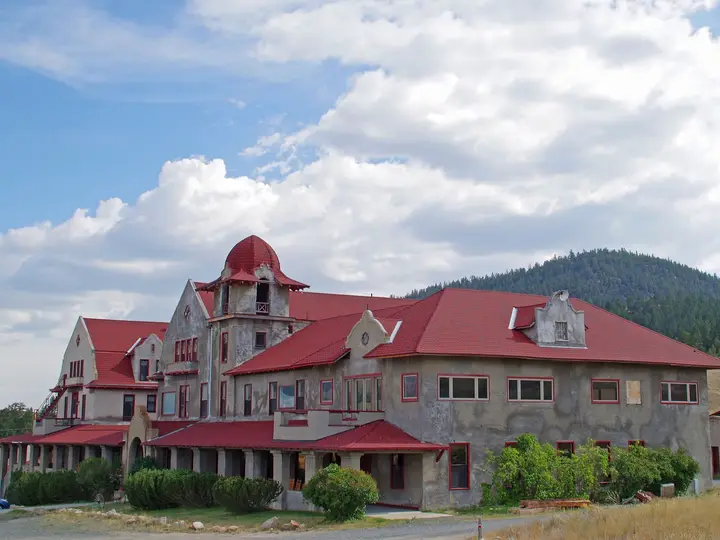 Historic Spanish Mission style Boulder Hot Springs Hotel with red roofs and a cupola under summer clouds