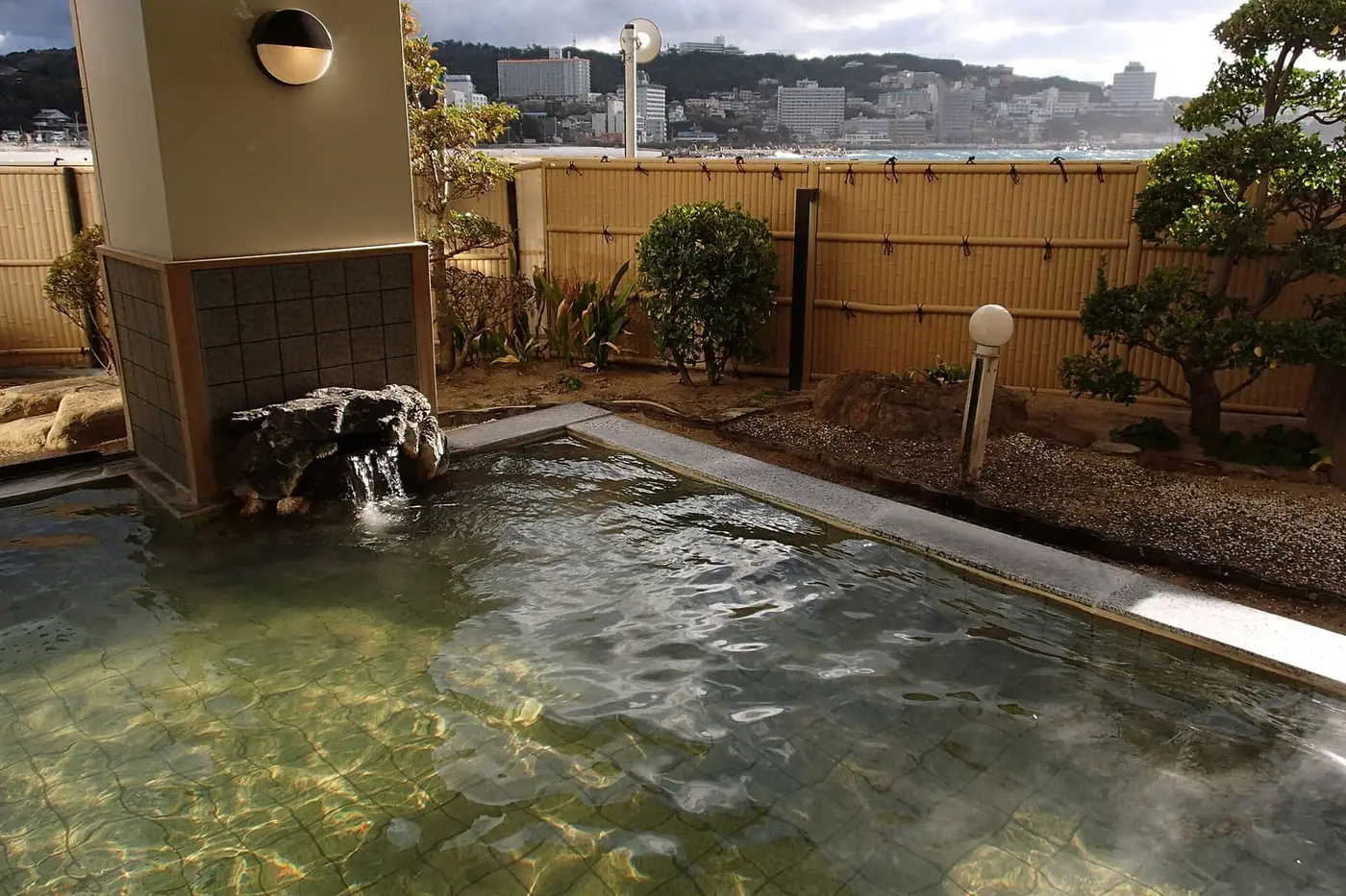 Rock lined outdoor hot spring pool at Shirahama Onsen with hotels and the coast beyond