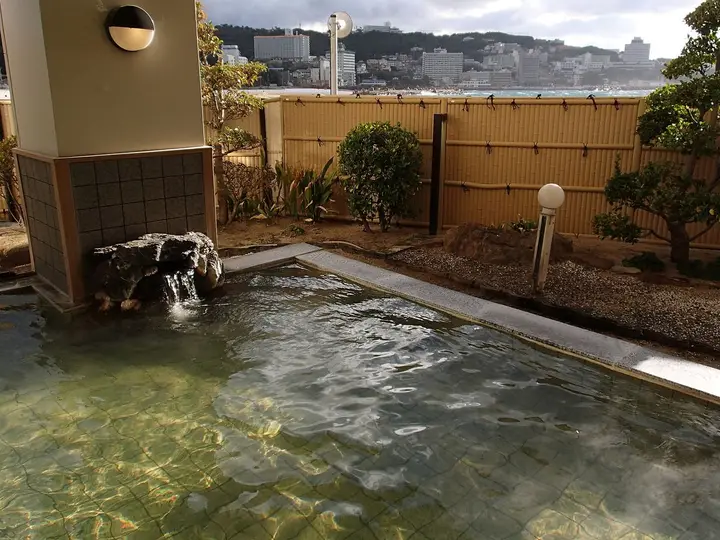 Rock lined outdoor hot spring pool at Shirahama Onsen with hotels and the coast beyond