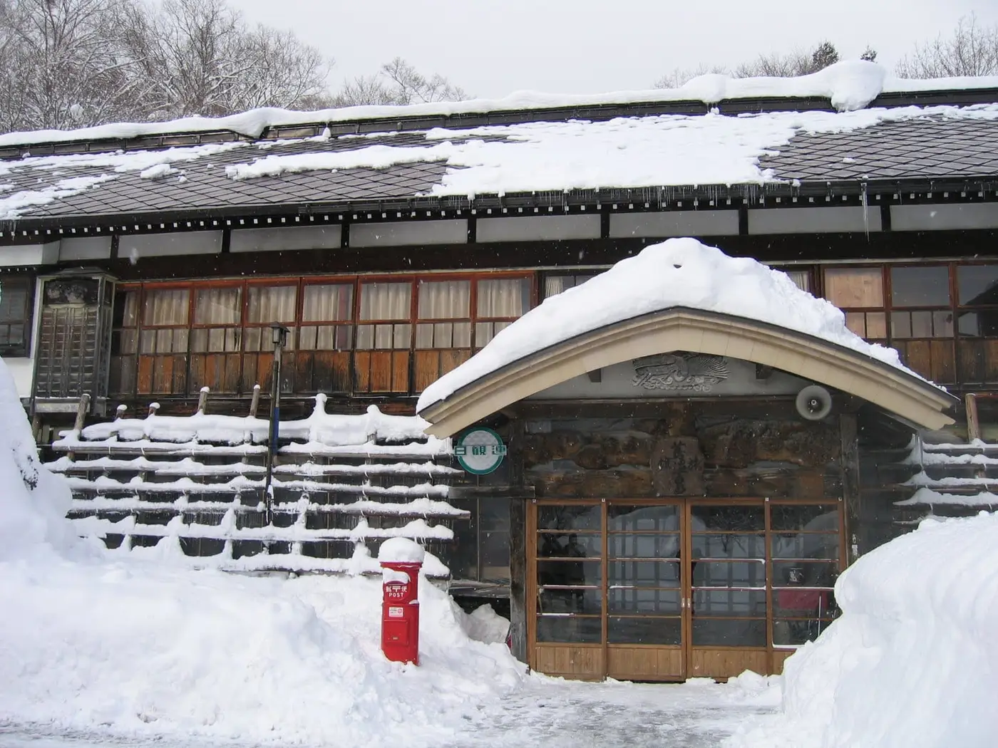 Snow covered wooden facade and entrance of Tsuta Onsen Ryokan in winter