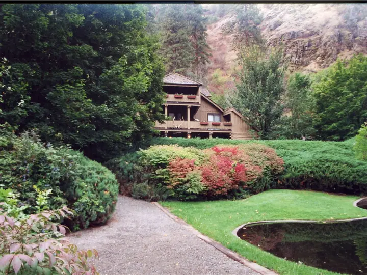 Wooden lodge at the former Riggins Hot Springs guest property behind gardens, lawn and a curved pond