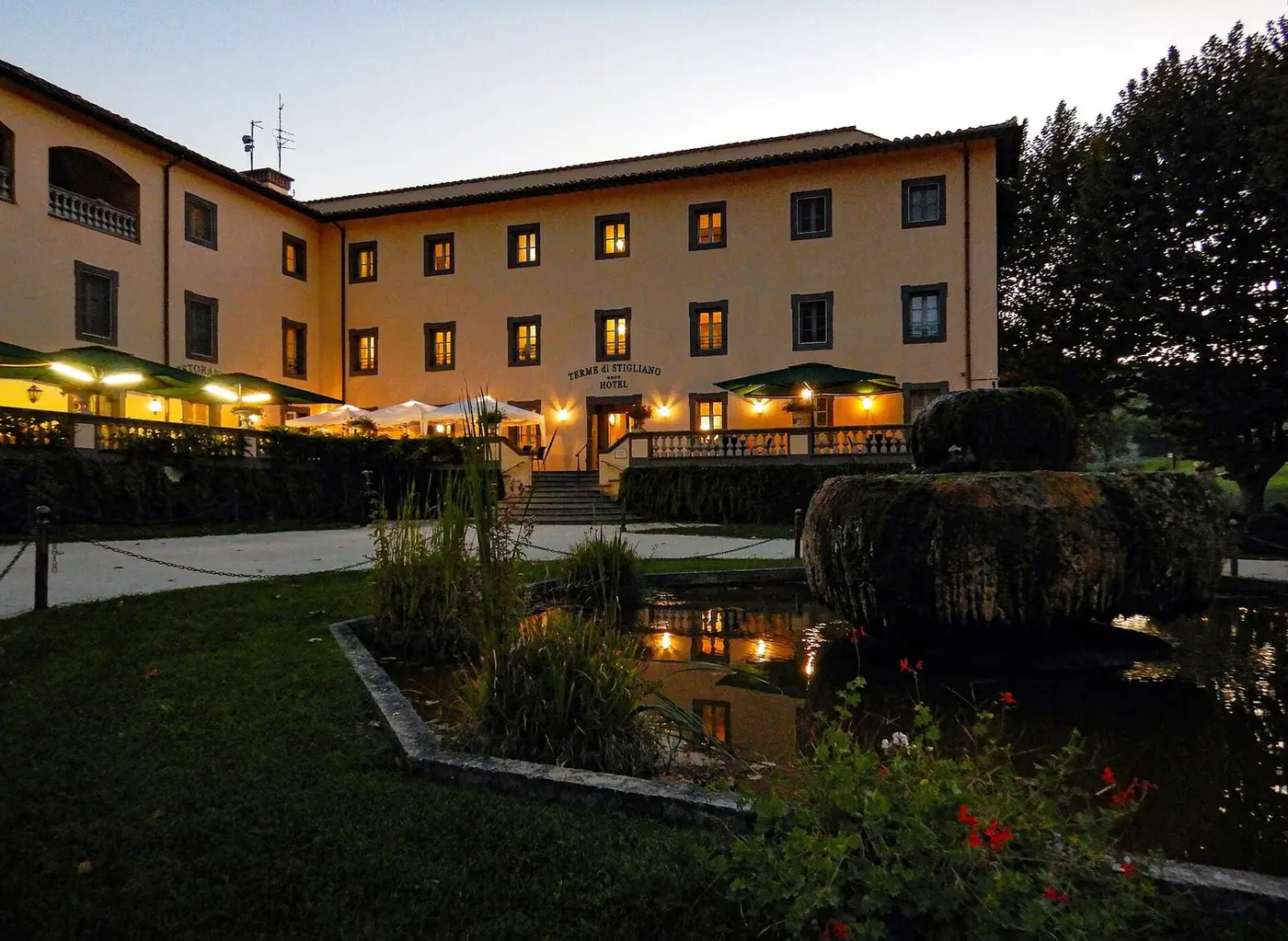 Terme di Stigliano hotel lit at dusk behind a garden pond and fountain