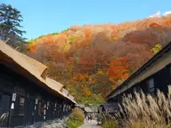 Thatched wooden lodge buildings of Tsurunoyu Onsen below a hillside of autumn foliage