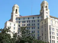 Twin towers of the historic Arlington Hotel rising above trees and a green lawn in Hot Springs