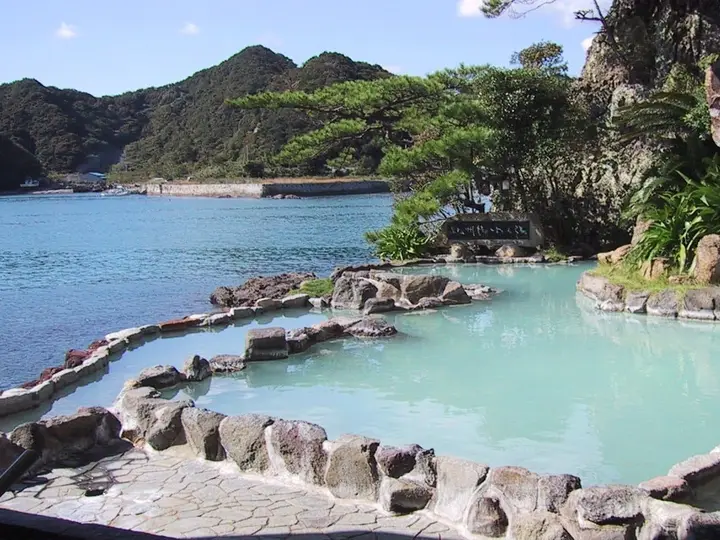 Milky blue outdoor onsen pool with rock edges overlooking the bay at Nakanoshima, Nachikatsuura
