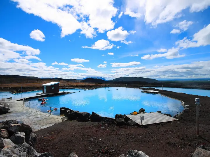 Milky blue geothermal lagoon at Mývatn with wooden decks and lava rocks under a bright sky