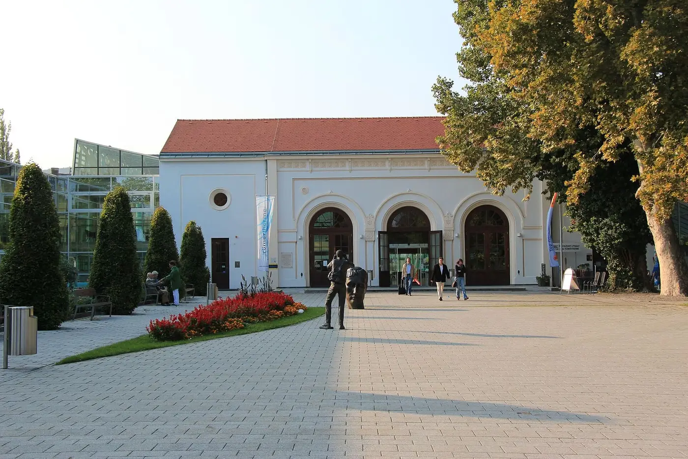 Paved forecourt and arched white entrance building of the Römertherme Baden beside its glass hall
