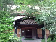 Wooden entrance of Awanoyu inn framed by green trees at Shirahone Onsen