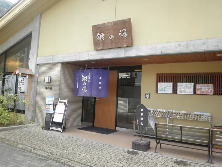 Entrance of Gin no Yu public bathhouse in Arima Onsen with its wooden sign and blue noren