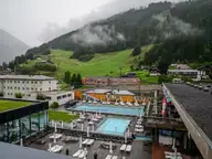 Outdoor thermal pools of the Felsentherme Bad Gastein below misty green mountain slopes