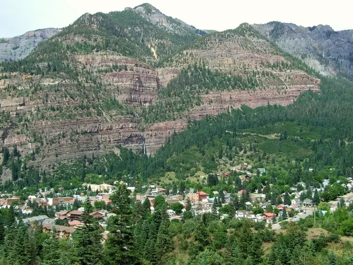 Ouray town tucked below steep red and green San Juan Mountain slopes, seen from Box Canyon