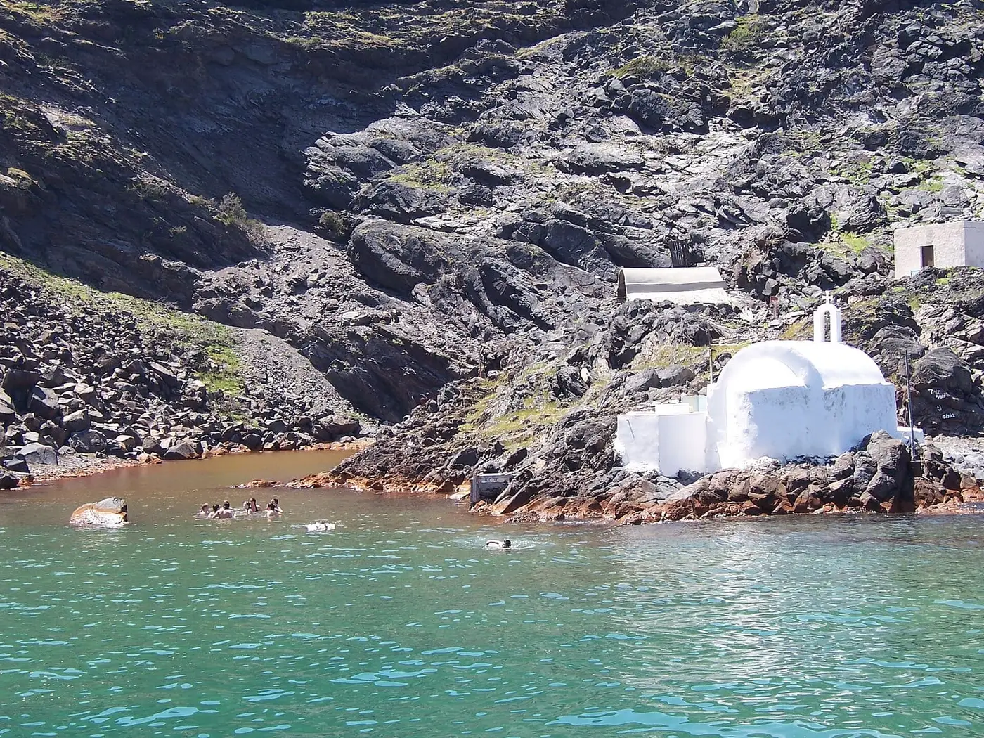 White chapel above the orange tinted hot spring bay of Palea Kameni in Santorini's caldera