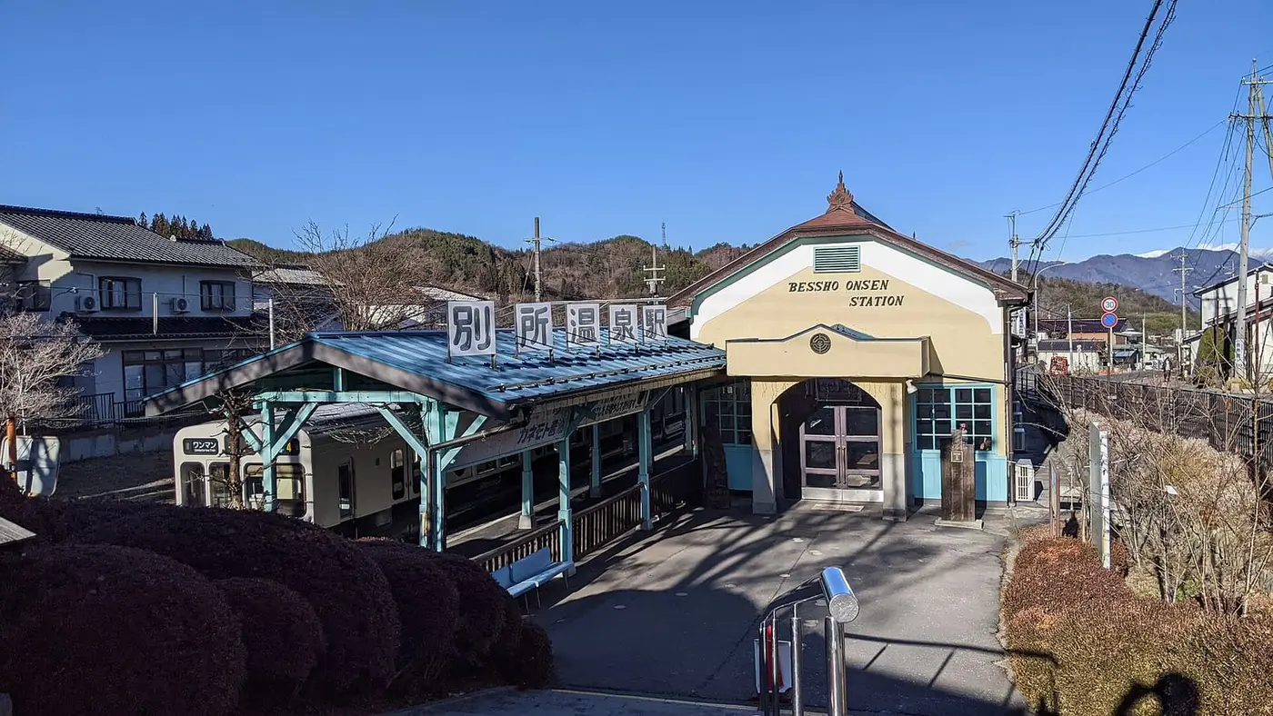 Retro Bessho Onsen Station with its blue platform roof below hills on a clear day
