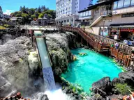 Turquoise hot water of the Kusatsu Onsen Yubatake pouring down a steaming channel beside wooden walkways