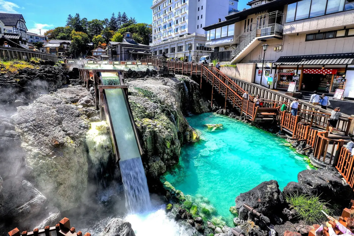 Turquoise hot water of the Kusatsu Onsen Yubatake pouring down a steaming channel beside wooden walkways