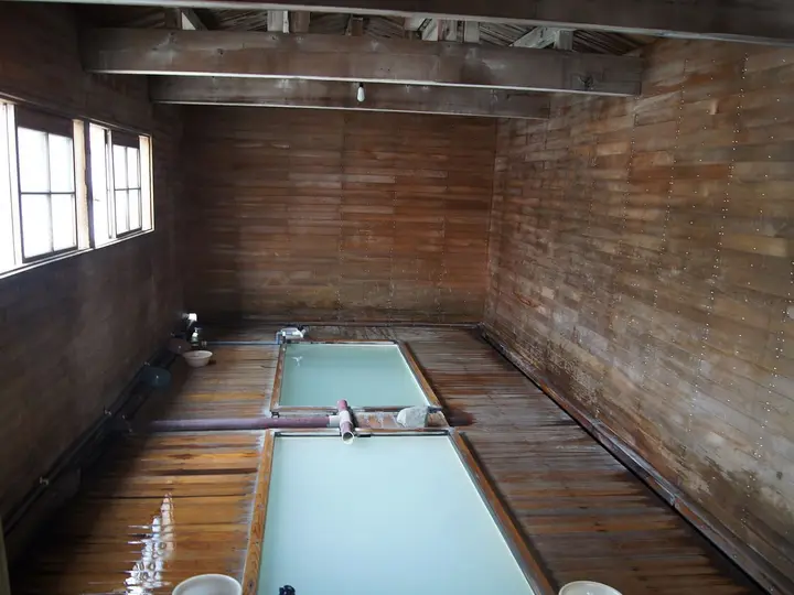 Wooden bath hut interior with pale blue sulfur water in a long tub at Osorezan Onsen