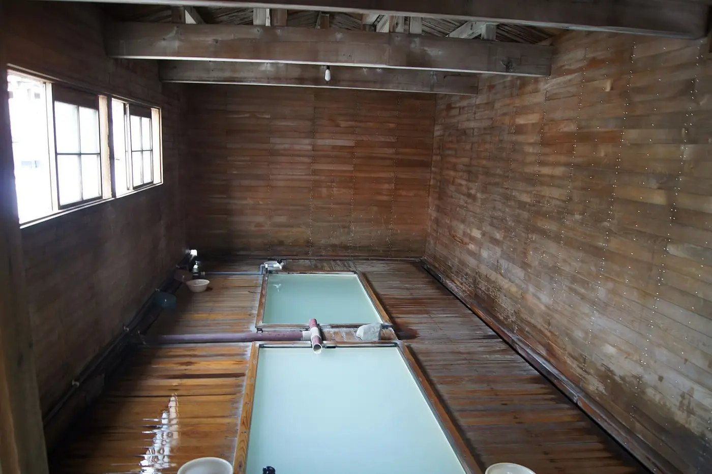 Wooden bath hut interior with pale blue sulfur water in a long tub at Osorezan Onsen