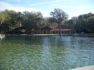 Clear swimming area of De Leon Springs with a roped line and red roofed park buildings beyond