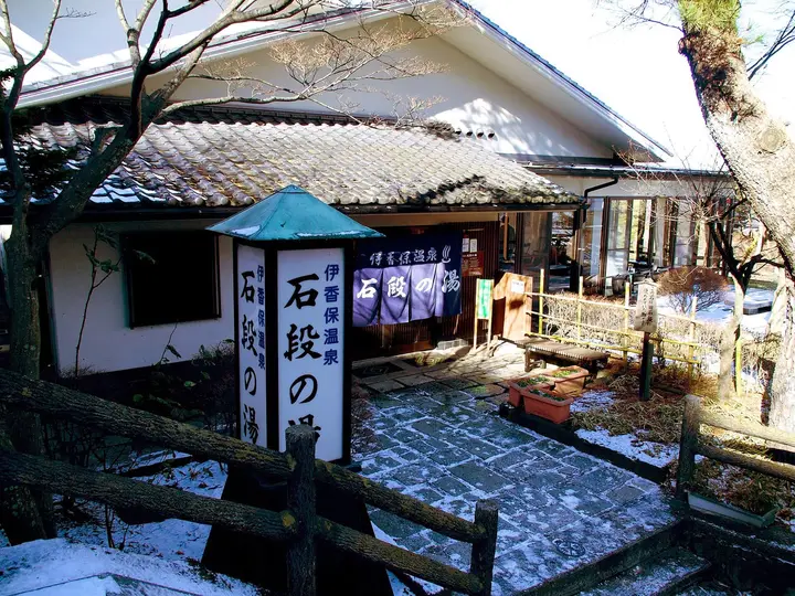 Ishidan no Yu public bathhouse at Ikaho Onsen with its tall wooden sign and light snow