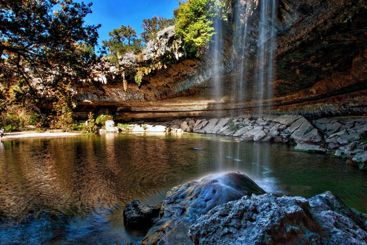 Waterfall pouring from a limestone overhang into the green grotto pool at Hamilton Pool Preserve